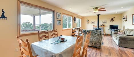 A dining area with a table set for four, wooden chairs, and a view through large windows.