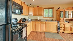 A kitchen with wooden cabinets, a black refrigerator, a microwave, and a stove. - Deck & Water View: Cozy Kentucky Lake Getaway (New Concord)