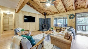 Een gezellig interieur van een chalet met houten wanden, een open haard, een televisie en een groot raam.