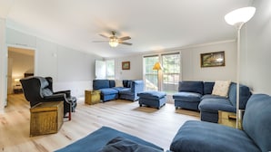 A spacious living room with a modern design, featuring a black leather sofa, blue armchairs, and a sectional sofa. There is a ceiling fan, a floor lamp, and a large window providing natural light. - North Carolina Home Near Mountain Biking & Fishing (Pisgah Forest)