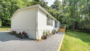 A single-story, white wooden house with a sloped roof, surrounded by a gravel driveway and a wooden deck. - North Carolina Home Near Mountain Biking & Fishing (Pisgah Forest)