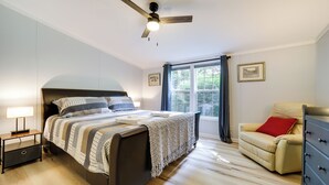 A bedroom with a bed, bedside table, nightstand, dresser, chair, window, and ceiling fan. - North Carolina Home Near Mountain Biking & Fishing (Pisgah Forest)
