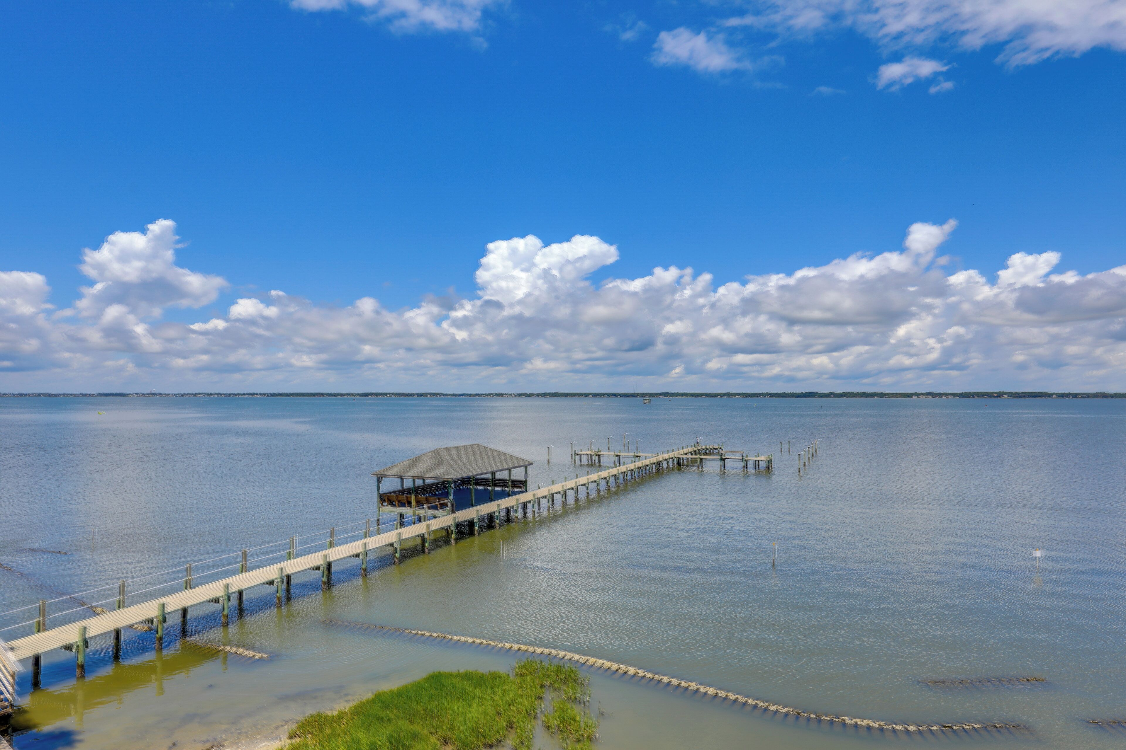 A pier extending into calm waters with a covered seating area and a clear sky.