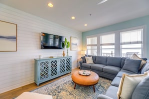 A living room with a grey sofa, a blue cabinet, a round coffee table, and a TV mounted on the wall. - Ocean Club Condo: Spectacular View & Beach Access! (Atlantic Beach)