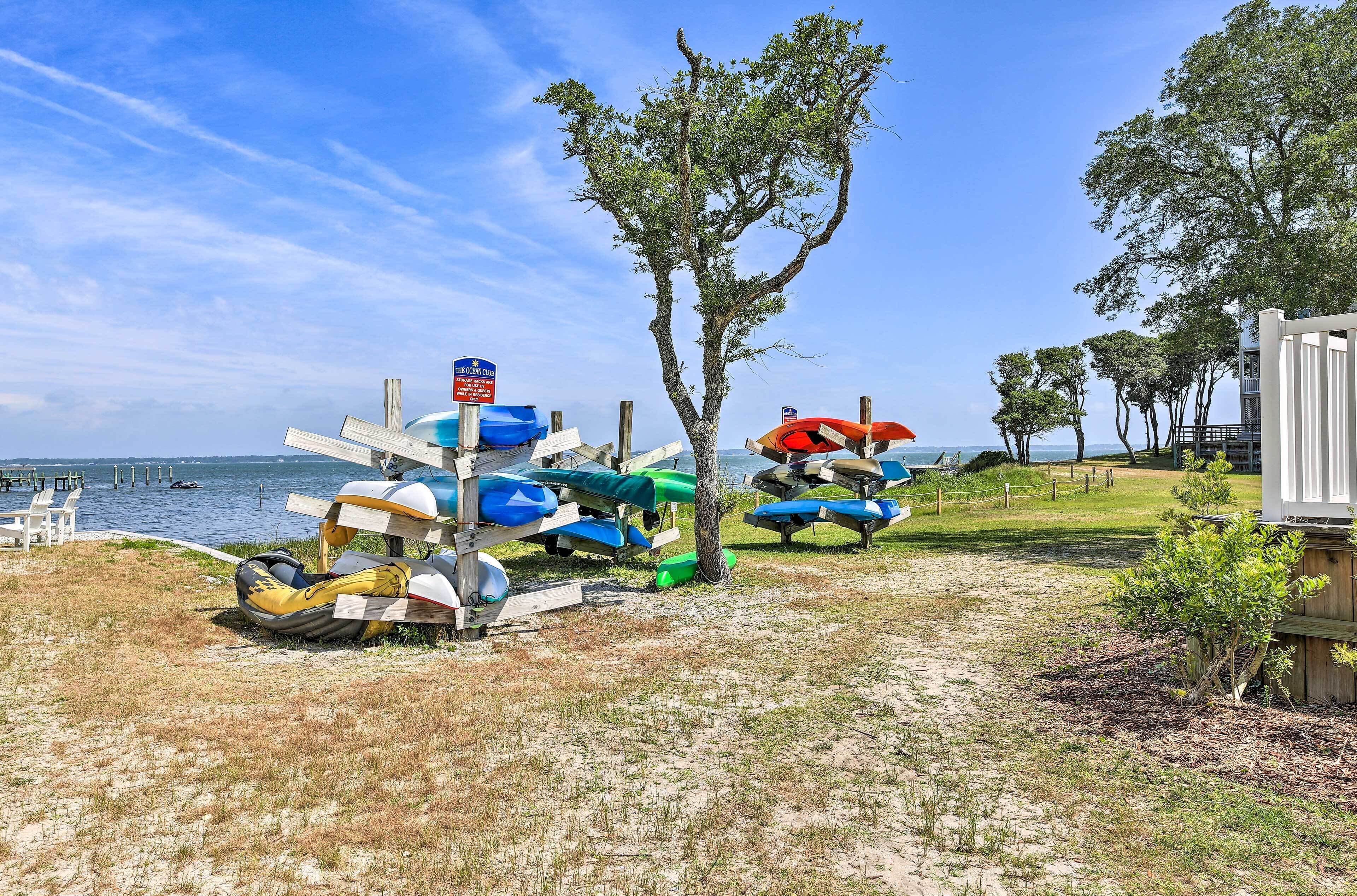 A beach area with several kayaks and canoes parked near the water, a tree, and a small building.