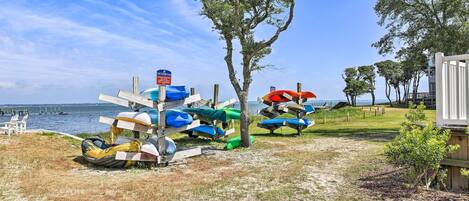 A beach area with several kayaks and canoes parked near the water, a tree, and a small building.