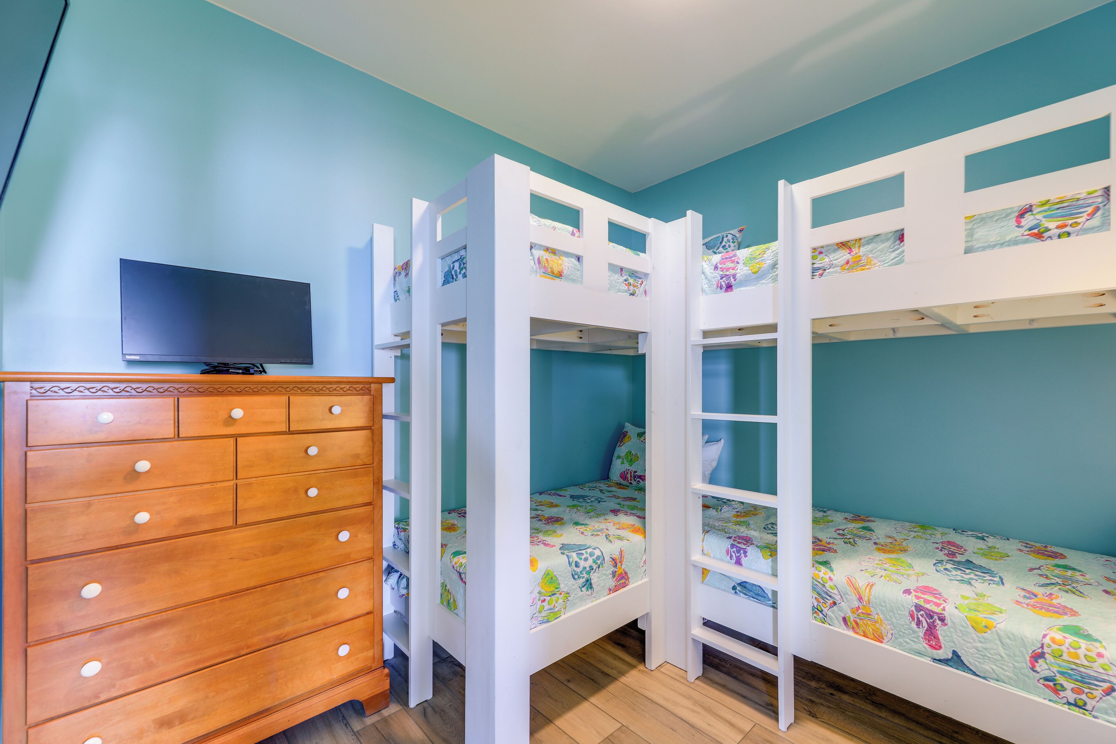 Un dormitorio con dos literas, un aparador de madera y un televisor en la pared.