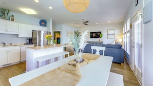 A modern kitchen with white cabinetry, a central island, and a dining area with a long table. - Ocean Club Condo: Spectacular View & Beach Access! (Atlantic Beach)