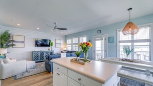 A spacious living room with a large white sofa, a blue sofa, and a kitchen area with a white island. - Ocean Club Condo: Spectacular View & Beach Access! (Atlantic Beach)