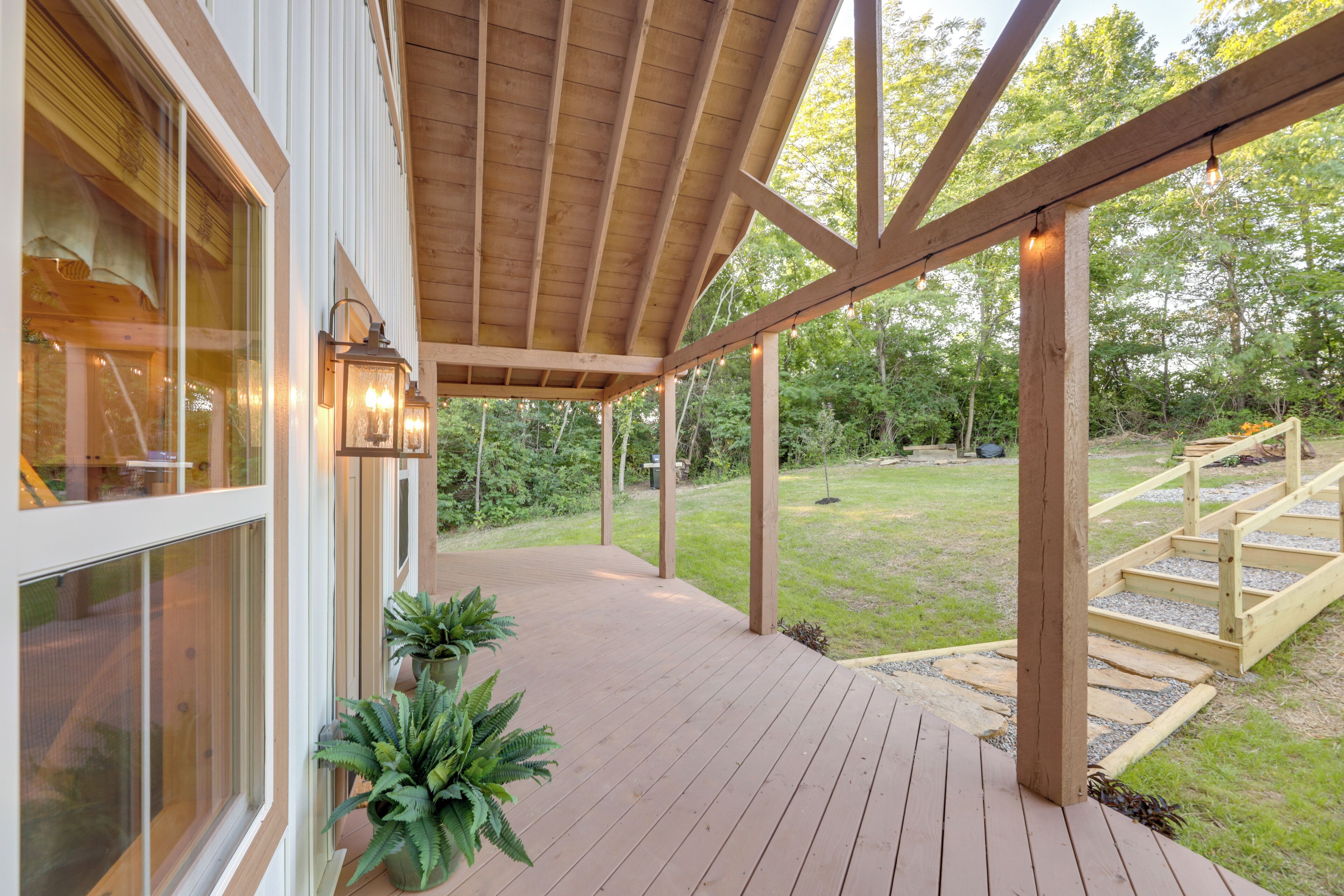 A wooden deck with a pergola, potted plants, and a view of a grassy yard.