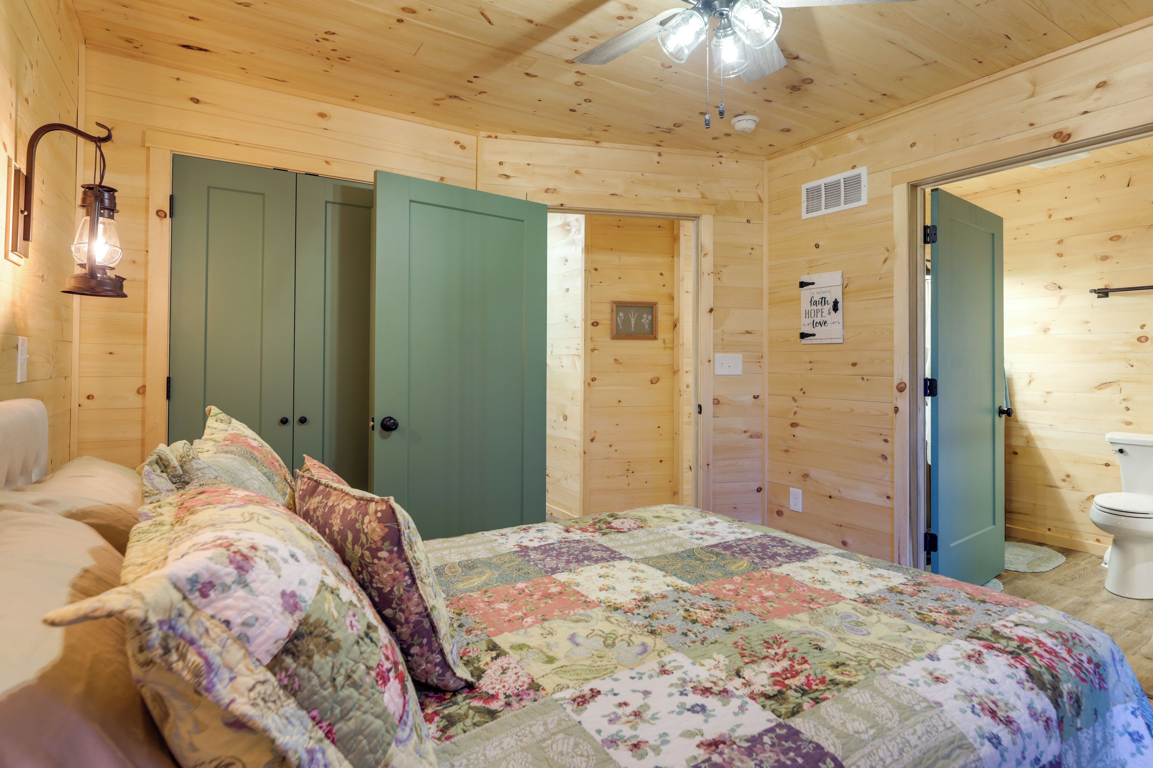 A wooden cabin bedroom with a bed, a green door, and a white toilet.