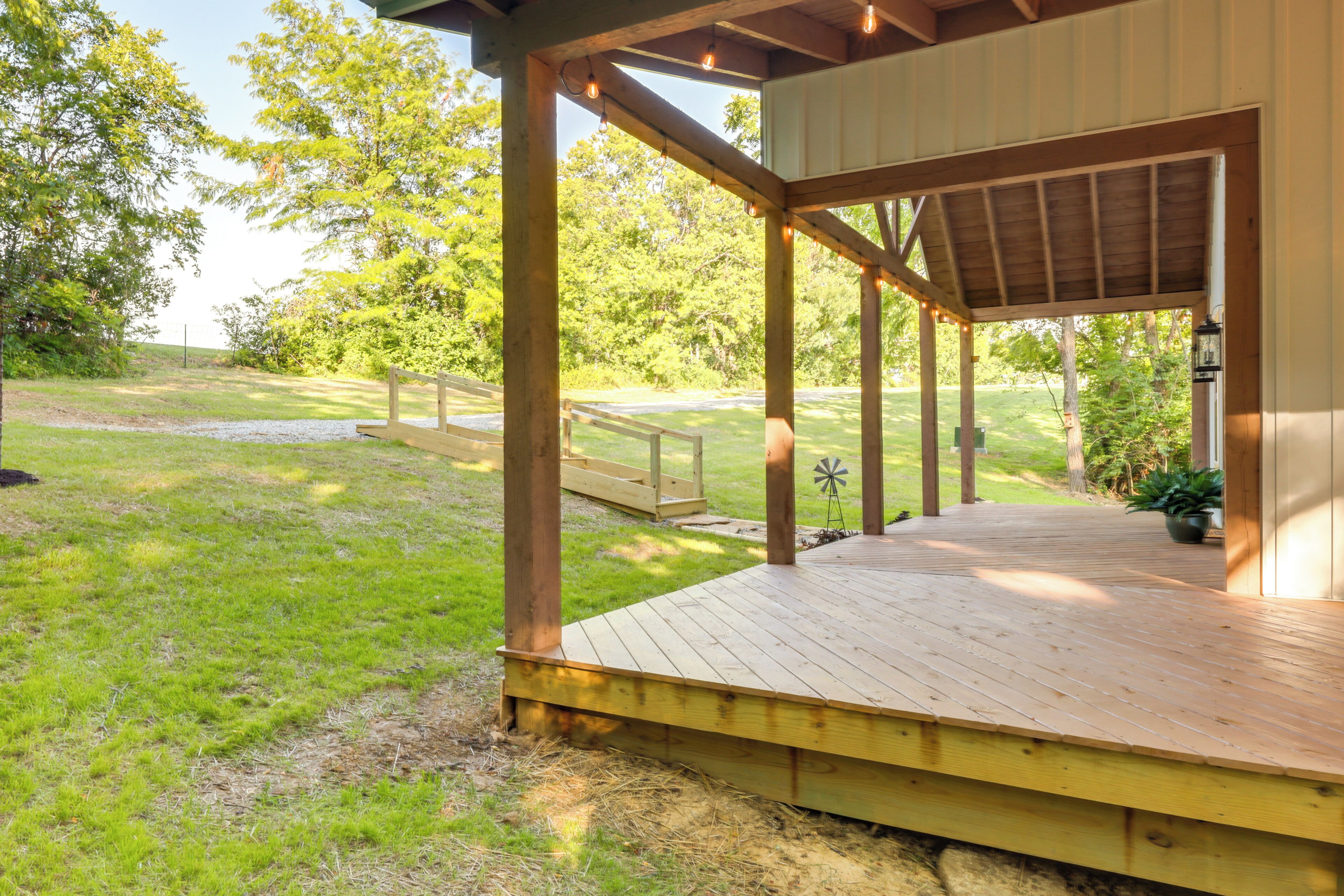 A wooden deck with a covered area, surrounded by a grassy lawn and trees.
