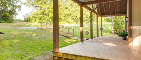 A wooden deck with a covered area, surrounded by a grassy lawn and trees.