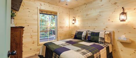 Une chambre dans une cabane en bois, avec un lit, un ventilateur de plafond, une fenêtre et une commode en bois.