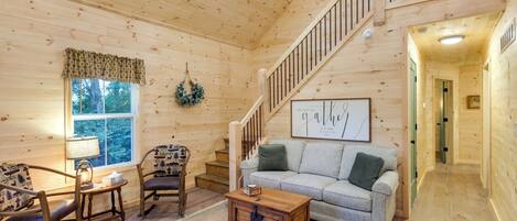 Un intérieur en bois avec un escalier, un canapé, une table basse et une fenêtre donnant sur des arbres.