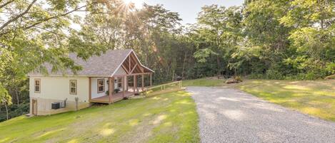 A two-story house with a porch, surrounded by a gravel driveway and lush greenery.