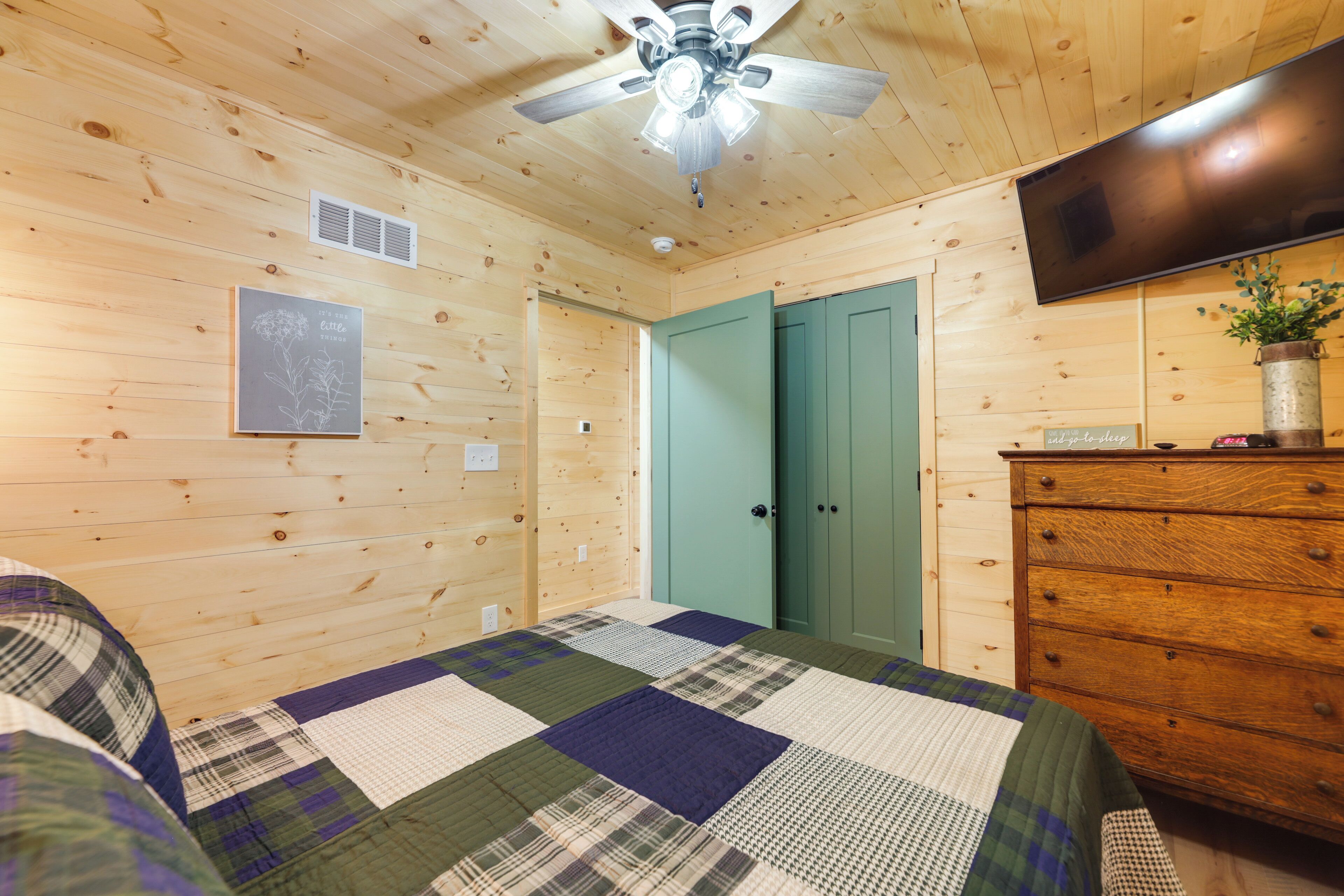 Een kamer met houten lambrisering, een bed, een dressoir, een plafondventilator en een aan de muur bevestigde televisie.