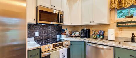 A kitchen with white cabinets, a stainless steel refrigerator, a microwave, a stove, and a dishwasher.