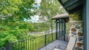 A balcony with a stone wall, a chair, and a view of a river surrounded by trees. - Riverfront Escape in Shawano on 3 Private Acres! (Shawano)