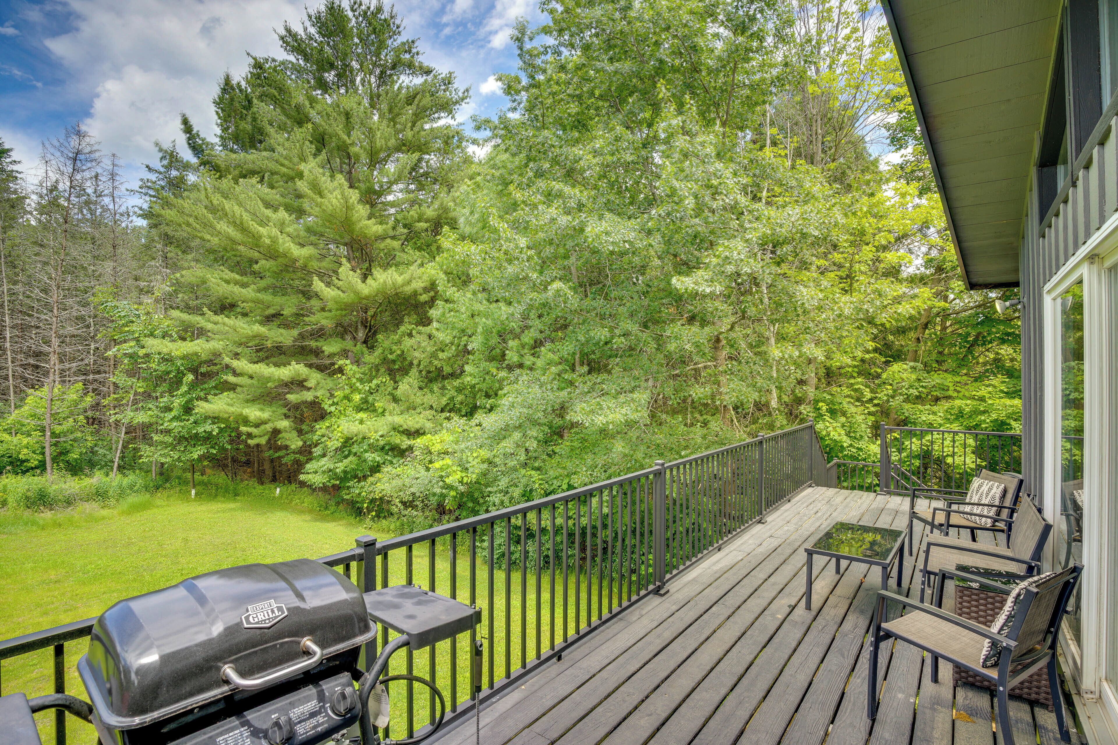 Eine Holzterrasse mit Grill, Gartenmöbeln und Blick auf ein bewaldetes Gebiet.