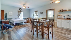 A spacious room with a bed, a dining table with chairs, a ceiling fan, a kitchen area with cabinets and a microwave, and a window with curtains. - Kentucky Retreat Near Williamstown Lake! (Williamstown)