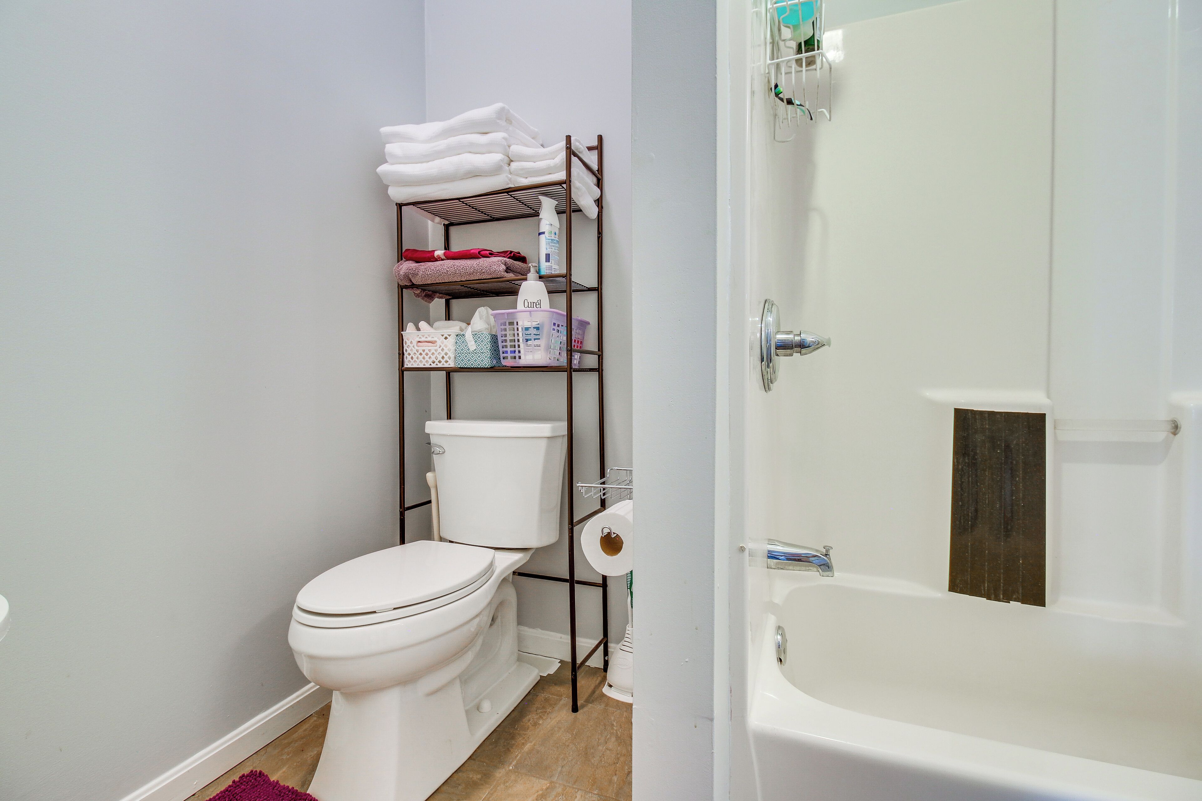 A bathroom with a toilet, a shelf with towels and toiletries, and a bathtub.