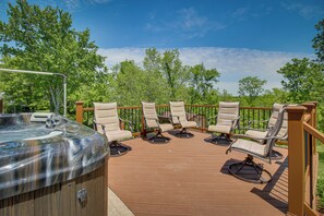 Een hottub omringd door zes loungestoelen op een houten terras met een balustrade, met uitzicht op een groen landschap.