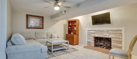 A living room with a sofa, a coffee table, a fireplace, a bookshelf, and a ceiling fan.