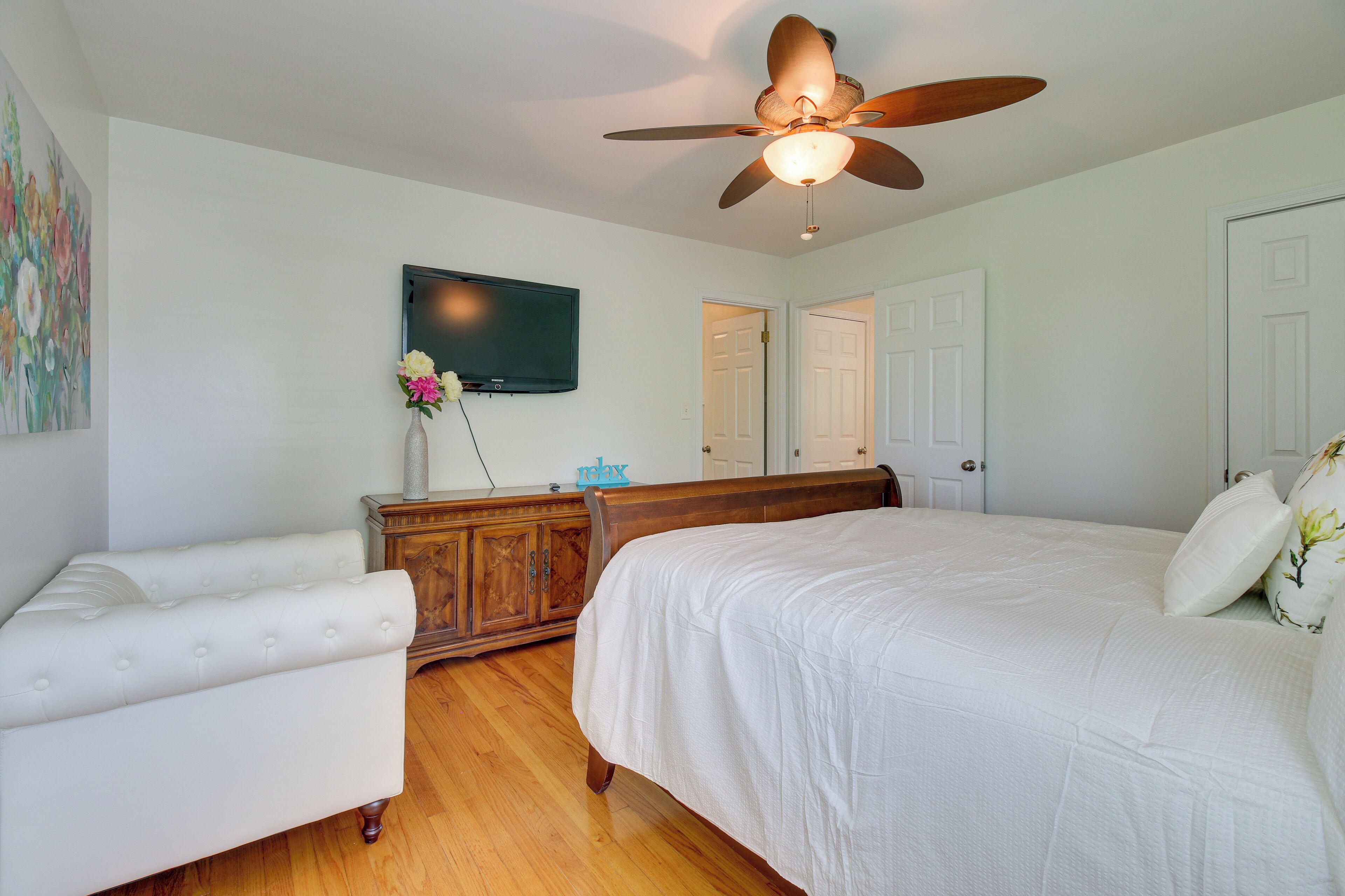 A bedroom with a bed, a dresser, a television, and a ceiling fan.