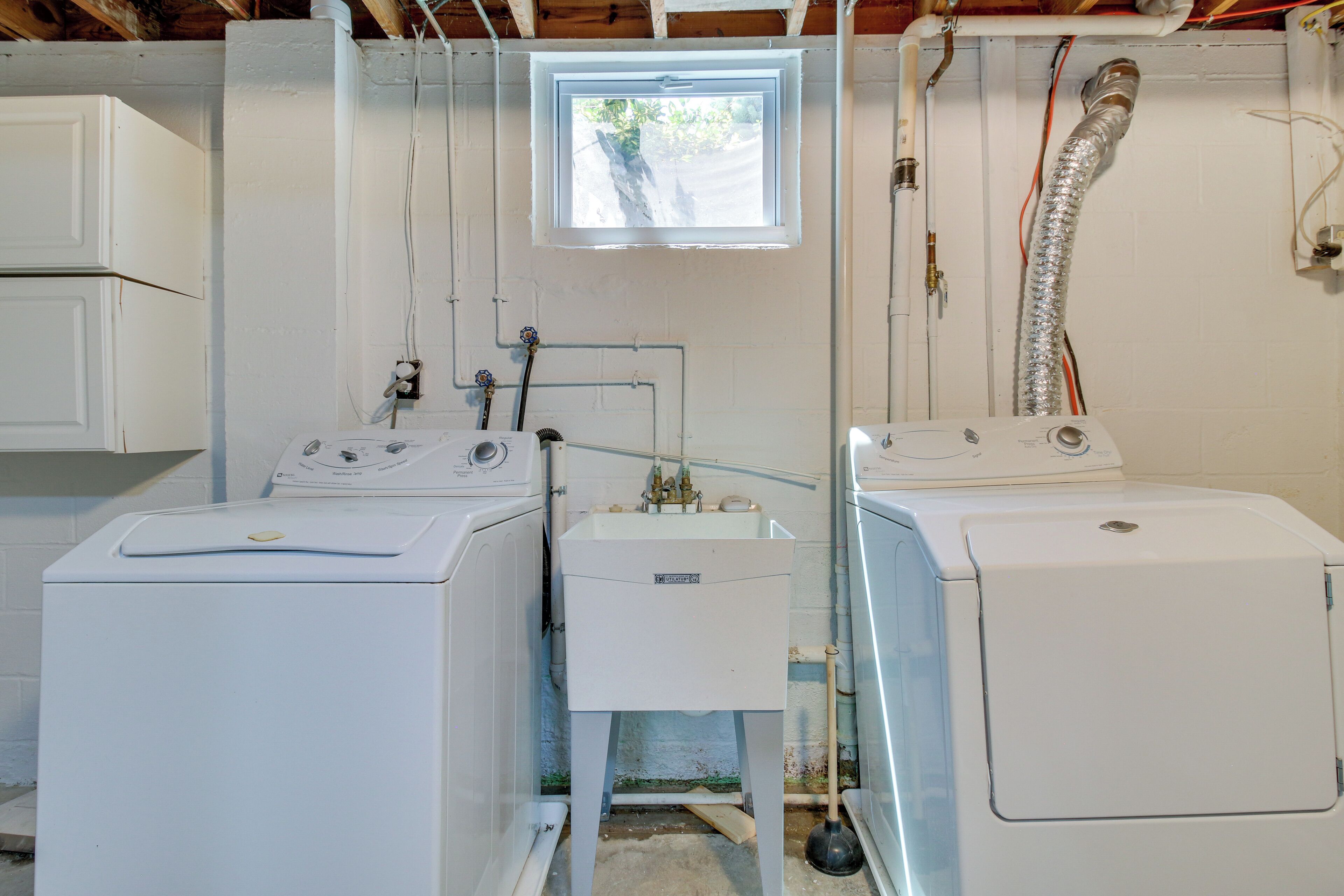 A laundry room with two washing machines, a water heater, and a window.