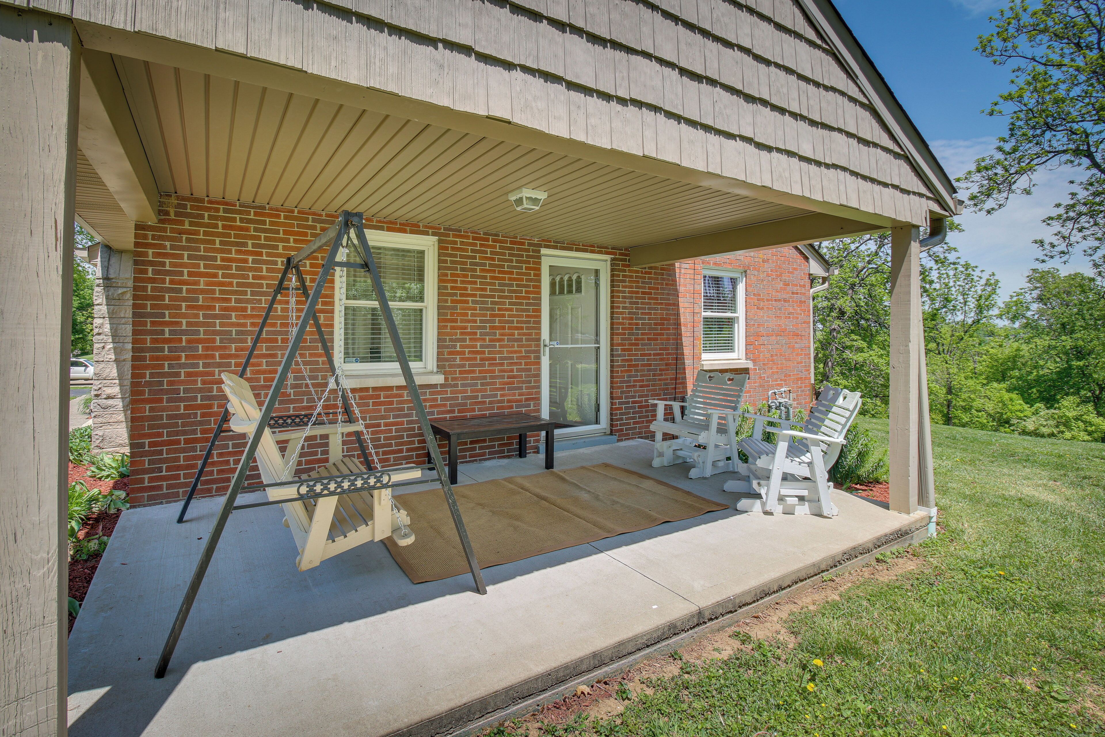 A covered porch with a swing set, two chairs, and a bench.