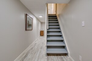 Un pasillo estrecho con piso de madera, una escalera con escalones blancos y un cuadro en la pared.