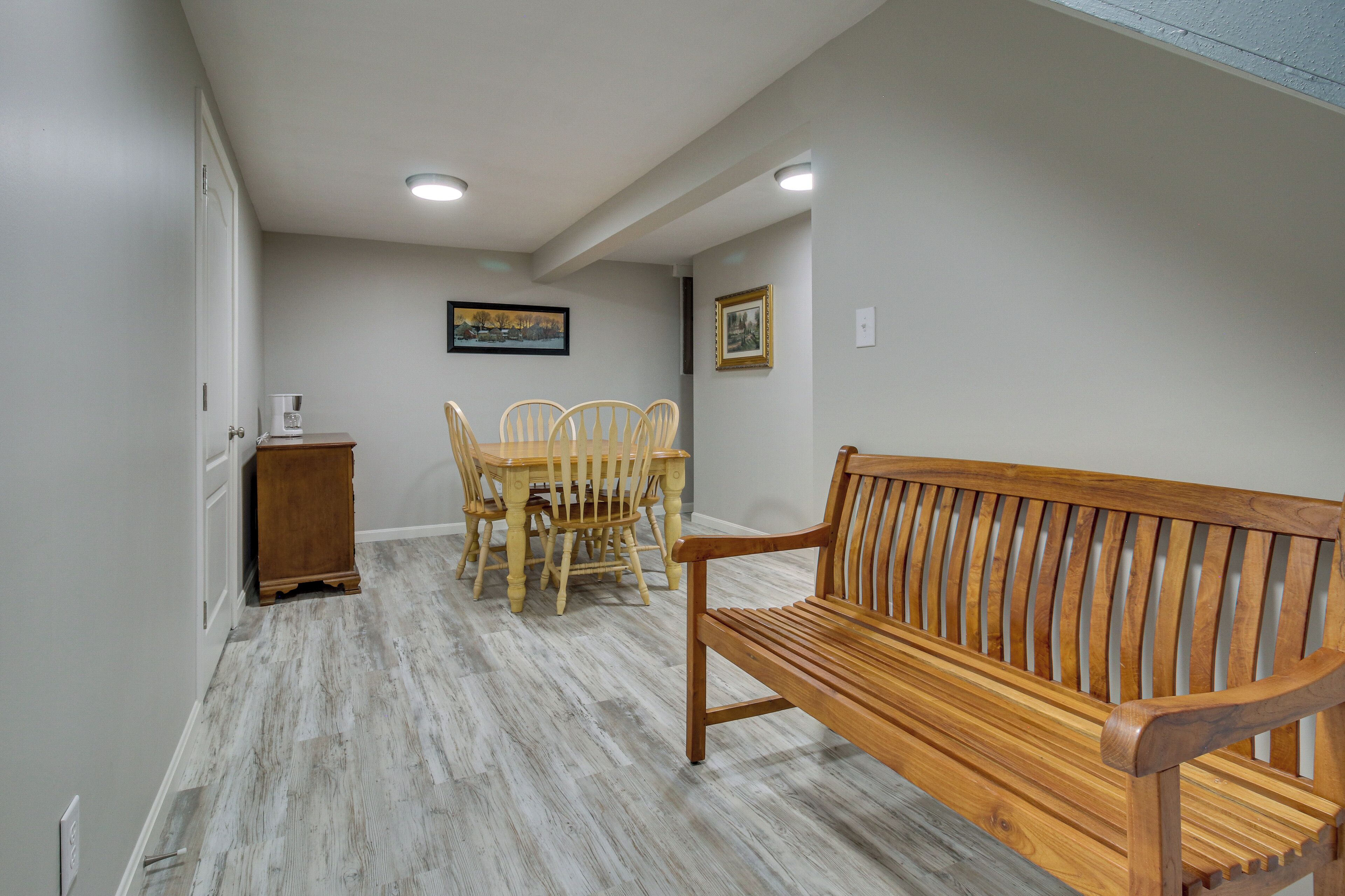 A room with a wooden bench, a dining table with chairs, and a small cabinet.