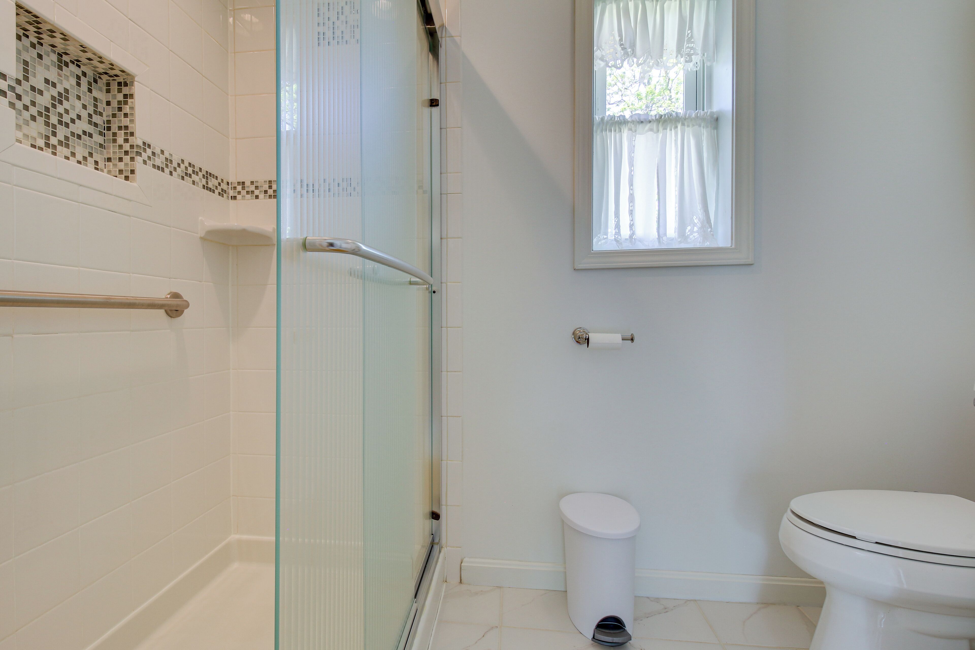 Ein Badezimmer mit Duschkabine aus Glas, Toilette und einem fensterbelaubten Fenster.