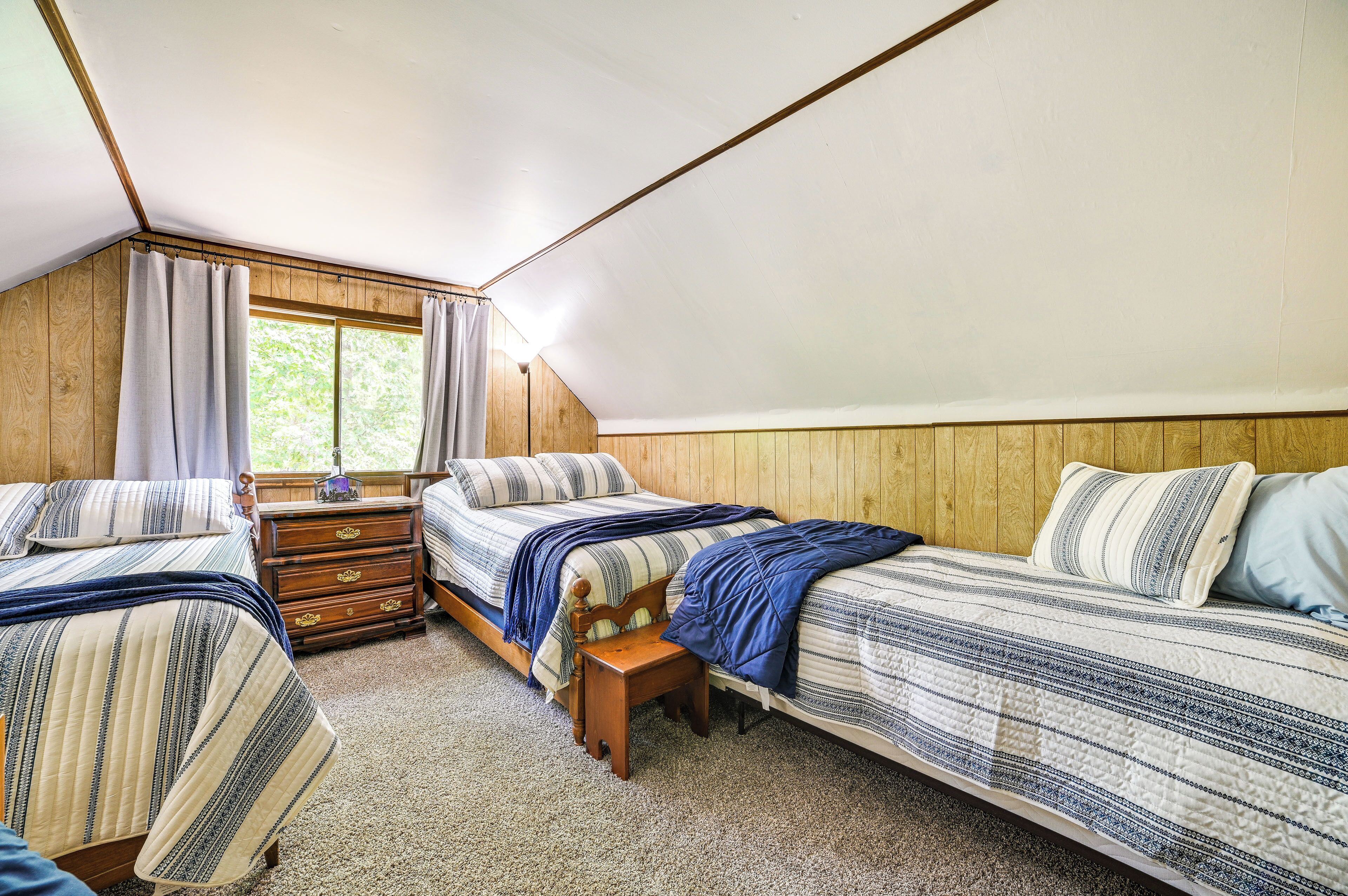 Un dormitorio con dos camas, un aparador de madera y un ventanal con cortinas.