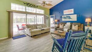 A living room with a sofa, coffee table, and chairs, a ceiling fan, and artwork on the walls.