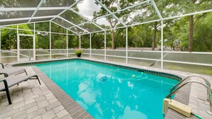 An indoor swimming pool with a glass enclosure, surrounded by a brick deck and equipped with lounge chairs.