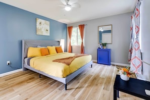 A bedroom with a bed, a ceiling fan, a nightstand, a mirror, and a window with curtains.