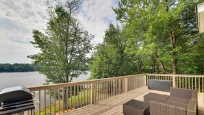 Ein Holzdeck mit Korbmöbeln, mit Blick auf einen See.