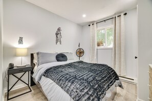 A bedroom with a bed, a bedside table with a lamp, a wall clock, and a window with curtains. - Community Perks: Family Poconos Home w/ Deck! (Tobyhanna)