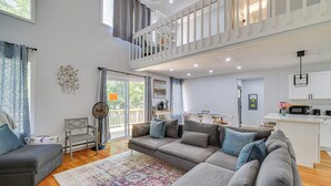 A spacious living area with a large gray sectional sofa, a small gray armchair, and a colorful rug. A balcony with a white railing is visible in the background. - Community Perks: Family Poconos Home w/ Deck! (Tobyhanna)