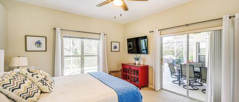 A bedroom with a bed, a ceiling fan, a TV, and a sliding glass door leading to an outdoor area.