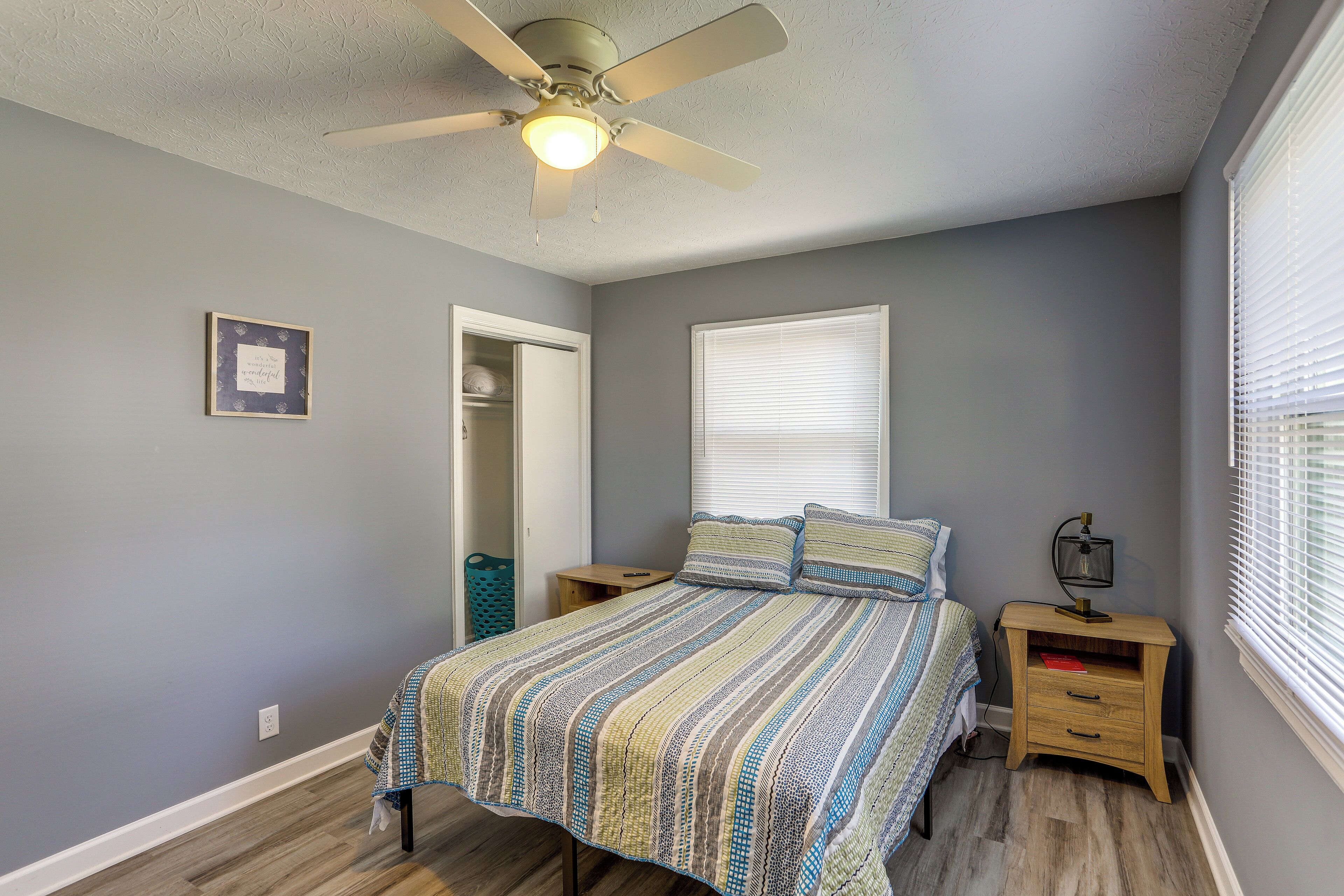 A bedroom with a bed, nightstands, a ceiling fan, a window with blinds, and a door leading to a closet.