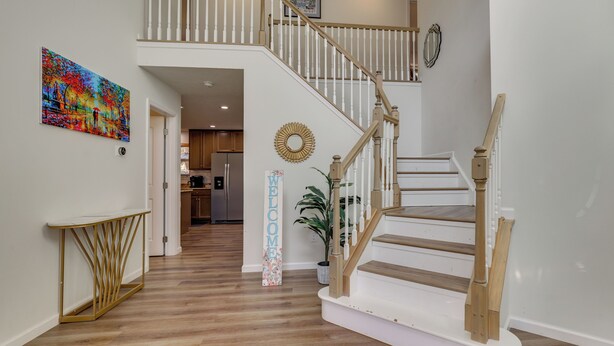 A staircase with wooden steps and white railings, leading to a second floor. A colorful painting and a welcome sign are visible on the walls. - Hot Tub + Lake Access: Spacious Tobyhanna Home (Tobyhanna)