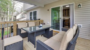 An outdoor deck with wicker furniture, a glass-top table, and a sliding glass door leading to a kitchen. - Hot Tub + Lake Access: Spacious Tobyhanna Home (Tobyhanna)