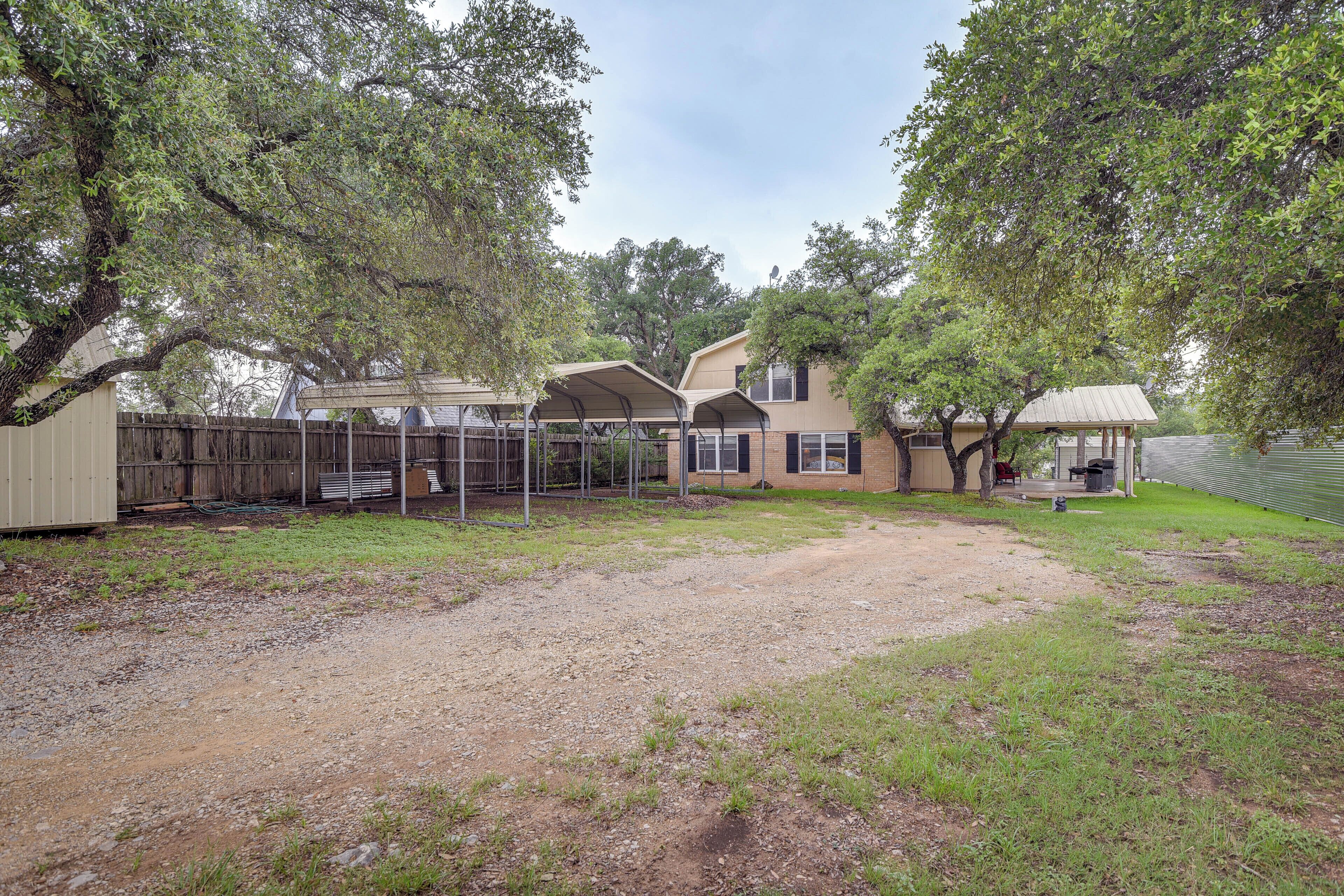 A fenced backyard with a covered patio area, a small shed, and a tree.