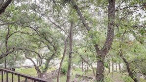 A wooden deck with a metal railing overlooking a wooded area with trees and a grassy field. - Lake Brownwood Home w/ Private Boat Dock! (Brownwood)