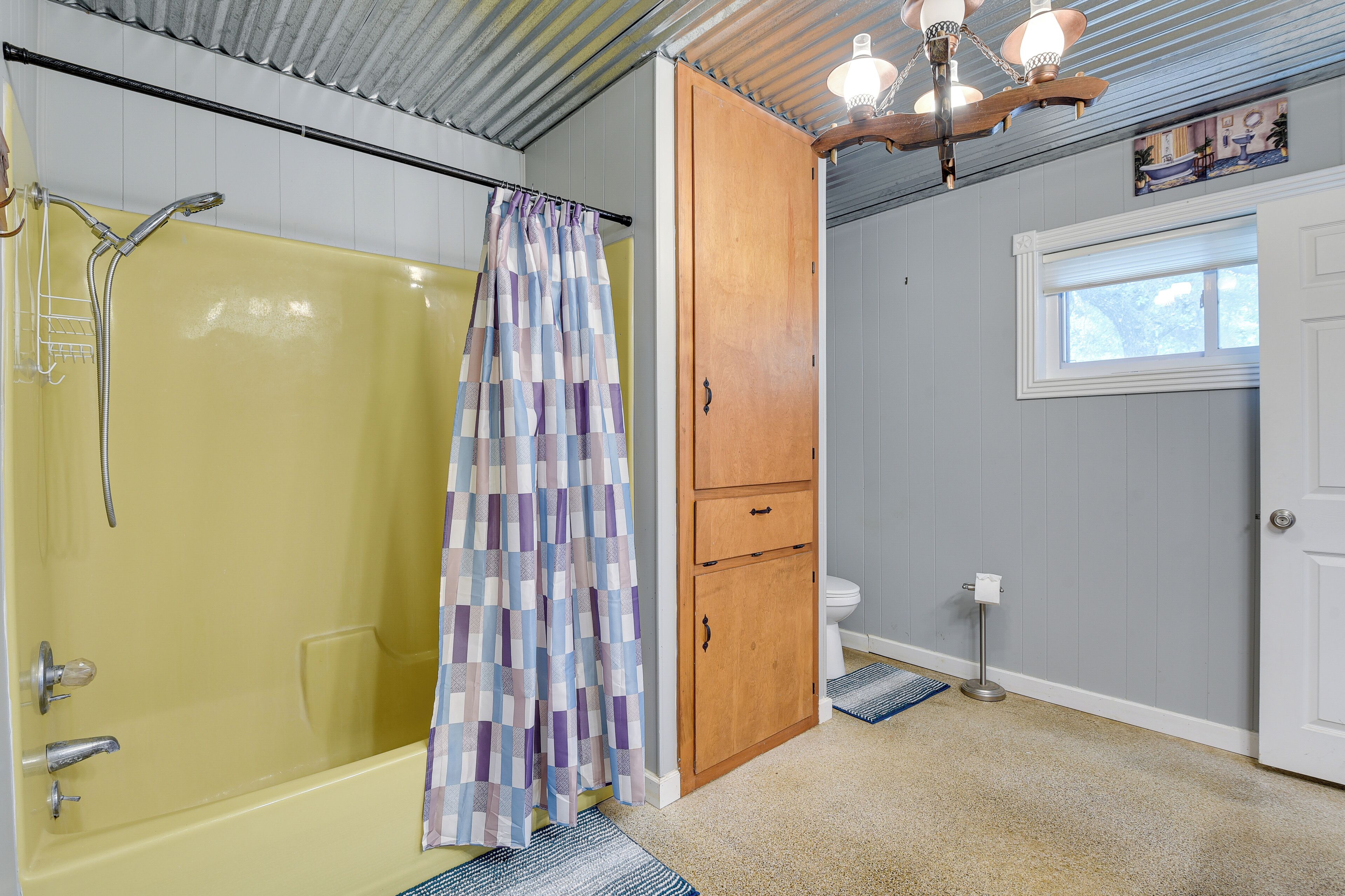 A bathroom with a yellow bathtub, a shower, a wooden cabinet, a toilet, and a window.