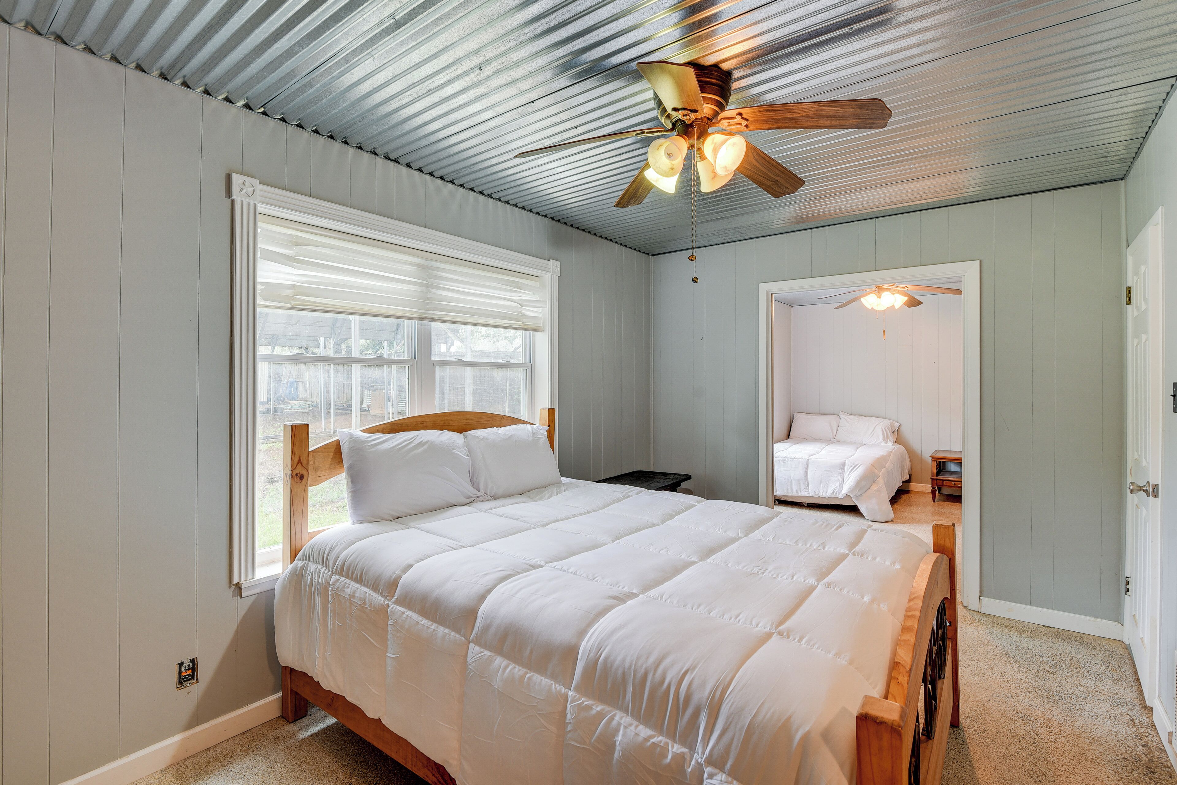 Ein Schlafzimmer mit einem hölzernen Bett, einem Deckenventilator und einem Fenster mit Jalousien.