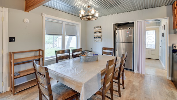 A modern kitchen with a dining area, featuring a large table, wooden chairs, a chandelier, and a refrigerator. - Lake Brownwood Home w/ Private Boat Dock! (Brownwood)